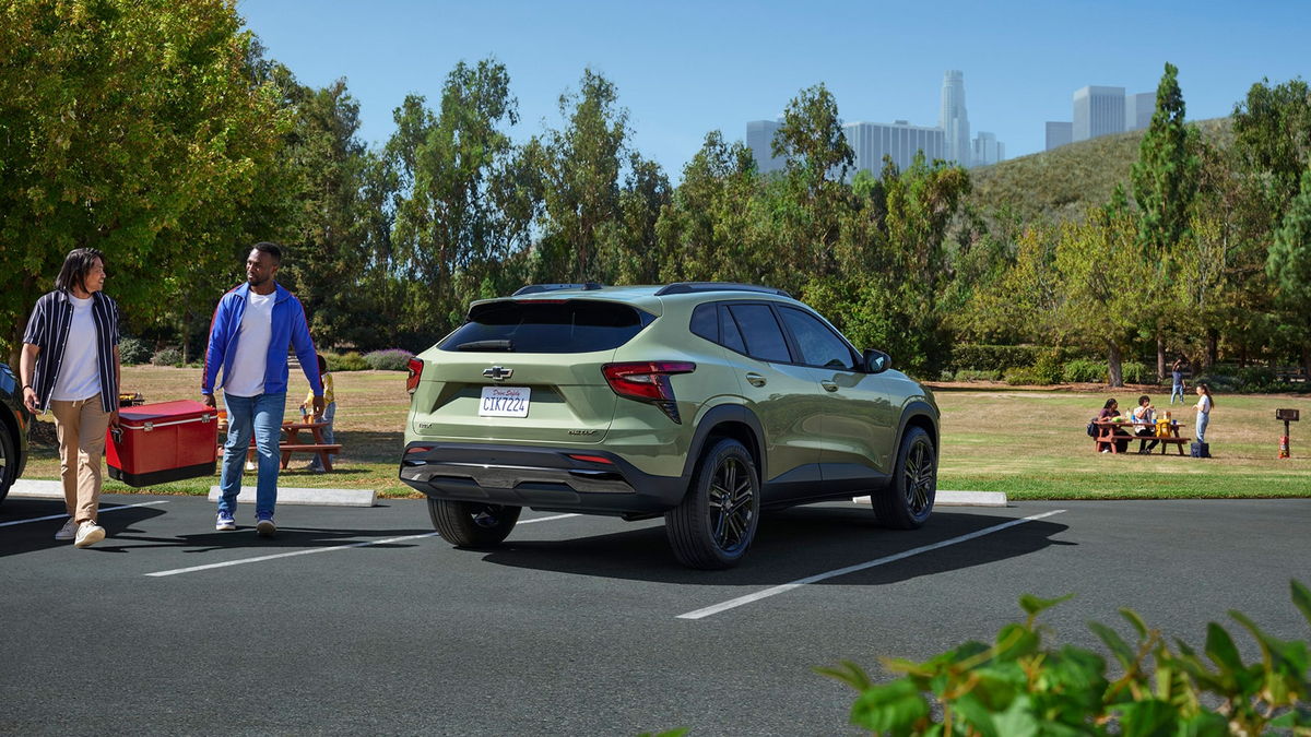 Two people loading a cooler into the rear of a 2026 Chevrolet Trax ACTIV at a park with a city skyline behind