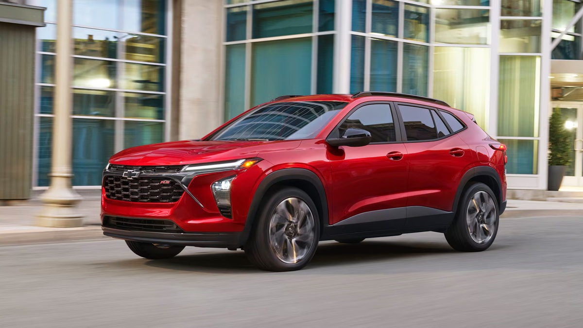 Red 2026 Chevrolet Trax RS parked outside a glass storefront, front three-quarter view